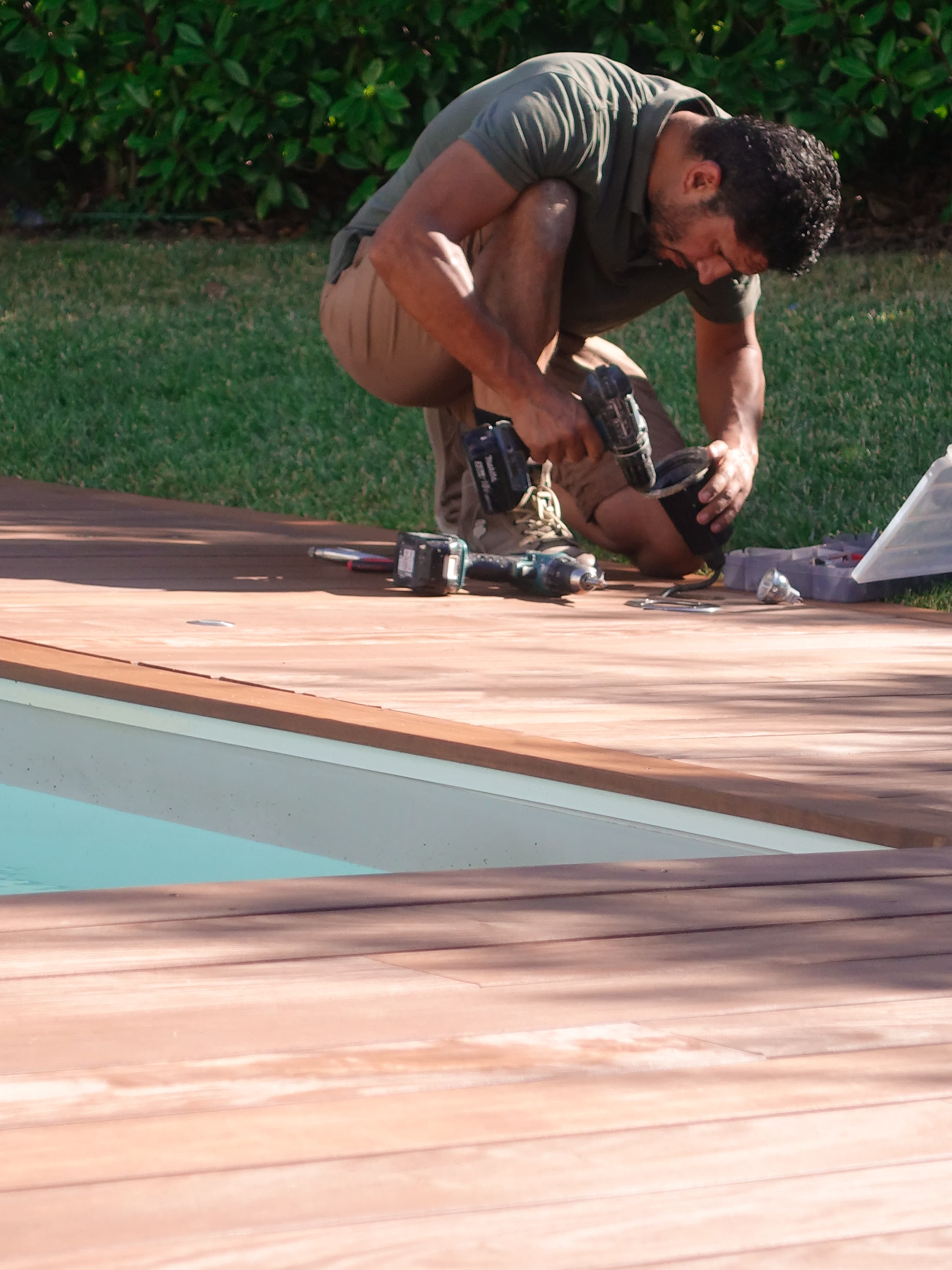 Un homme installe des éclairages extérieurs sur une terrasse de piscine, entourée d'une pelouse verte luxuriante, pour illuminer élégamment la zone de la piscine.